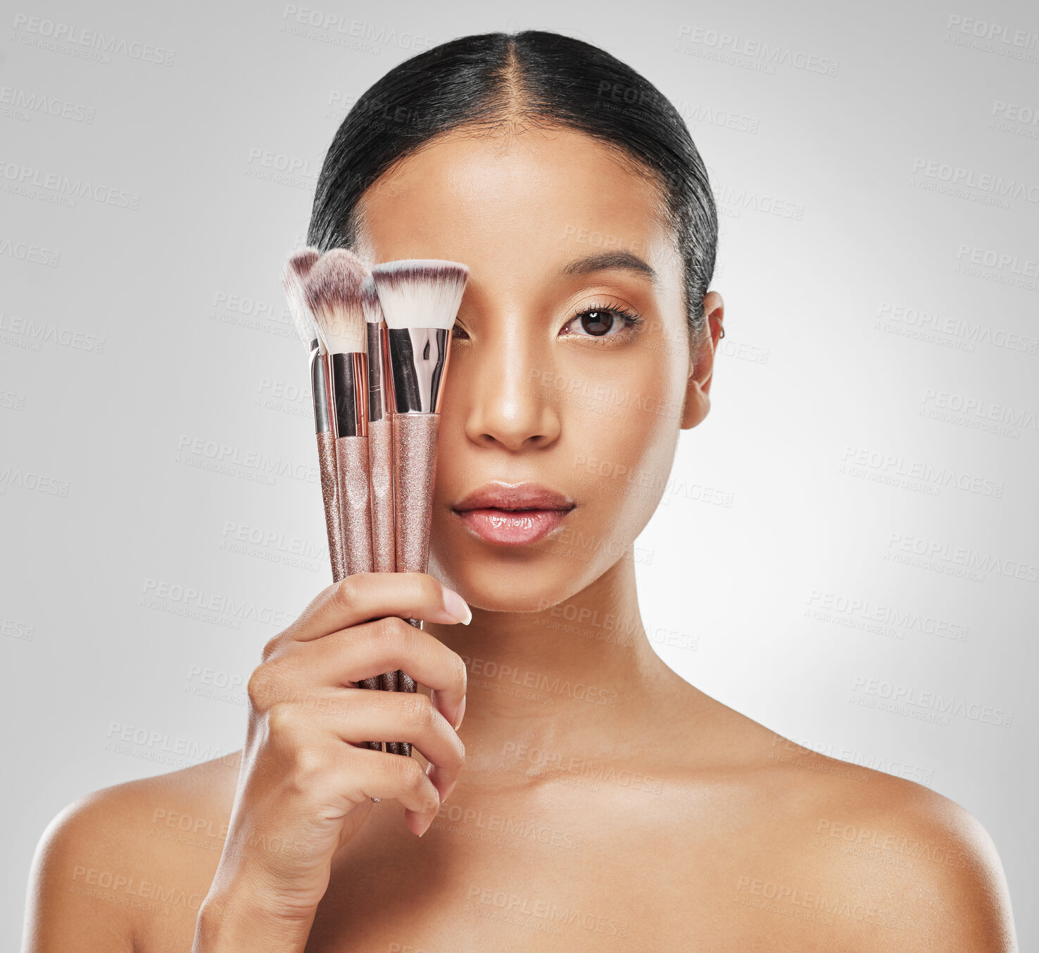 Buy stock photo Studio portrait of an attractive young woman holding a collection of makeup brushes against a grey background