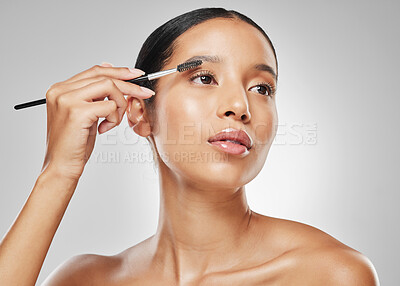 Buy stock photo Studio shot of an attractive young woman using an spoolie brush to comb her eyebrows against a grey background