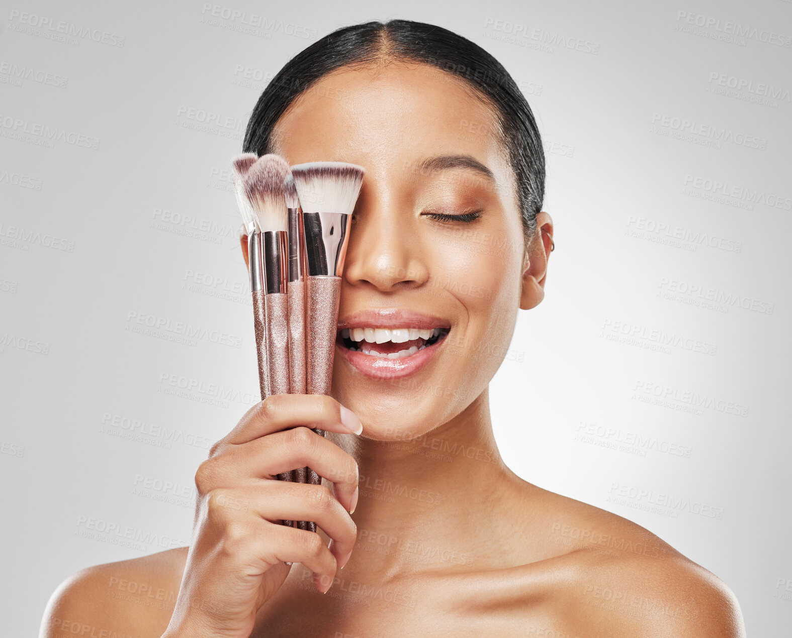 Buy stock photo Studio shot of an attractive young woman holding a collection of makeup brushes against a grey background