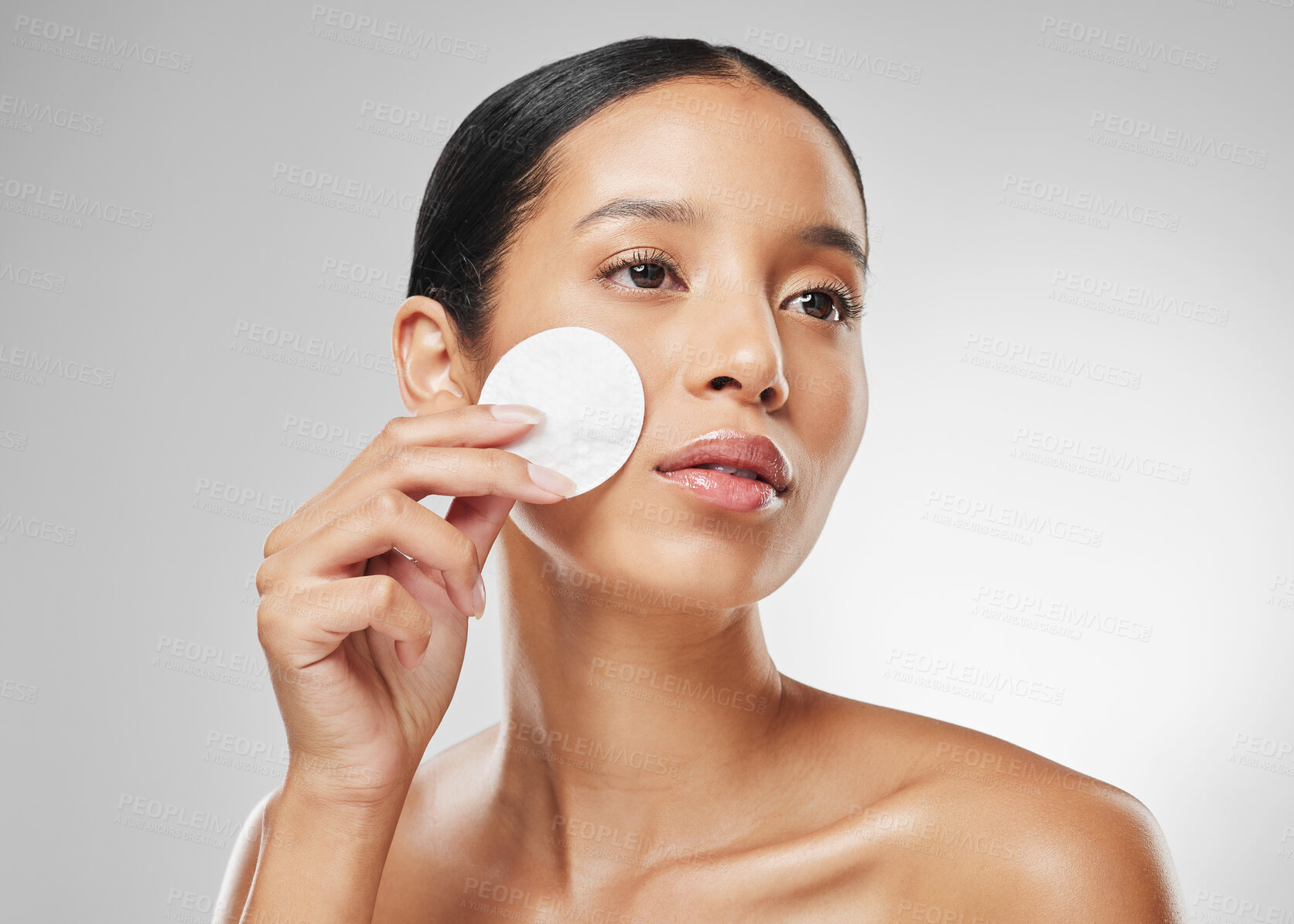 Buy stock photo Studio shot of an attractive young woman using a cotton pad on her face against a grey background