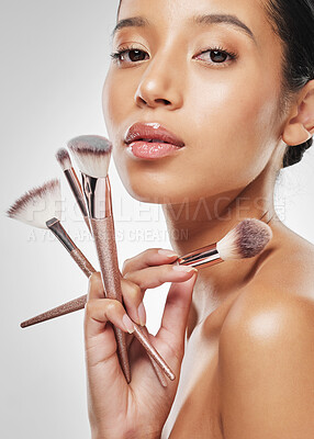 Buy stock photo Studio portrait of an attractive young woman holding a collection of makeup brushes against a grey background