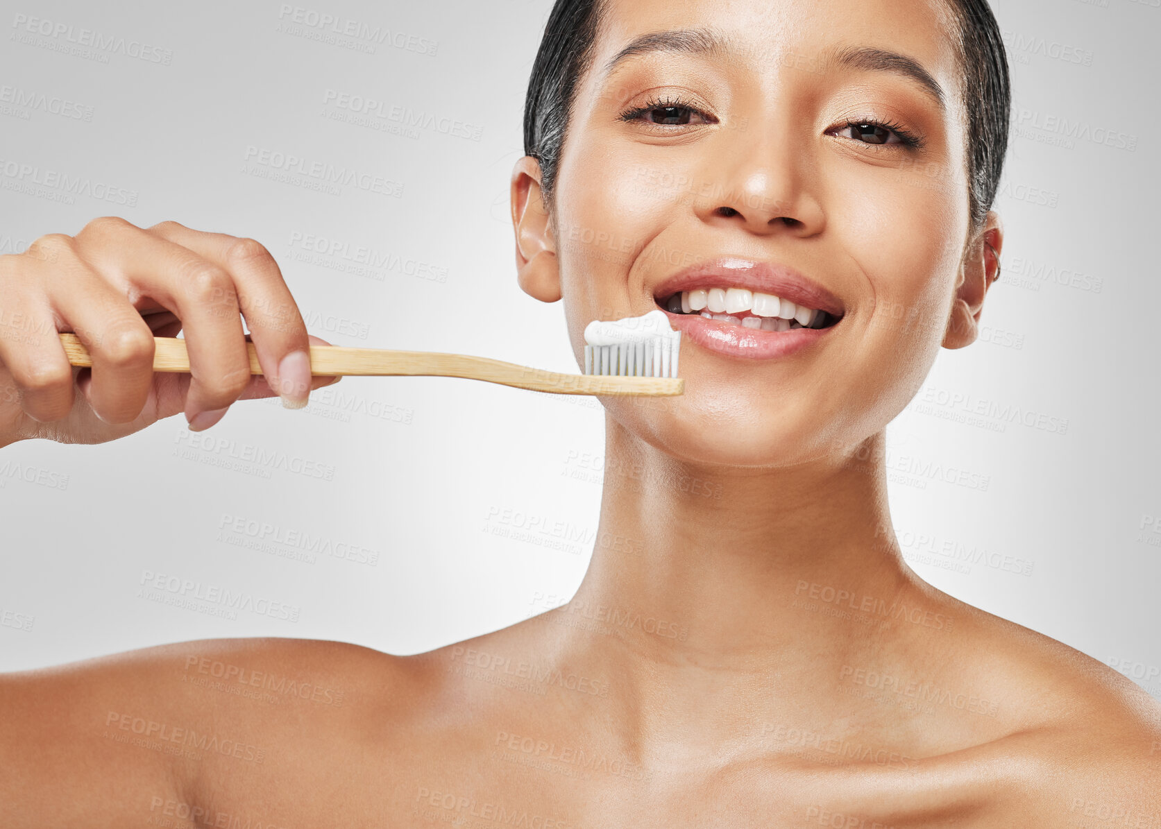 Buy stock photo Studio portrait of an attractive young woman brushing her teeth against a grey background