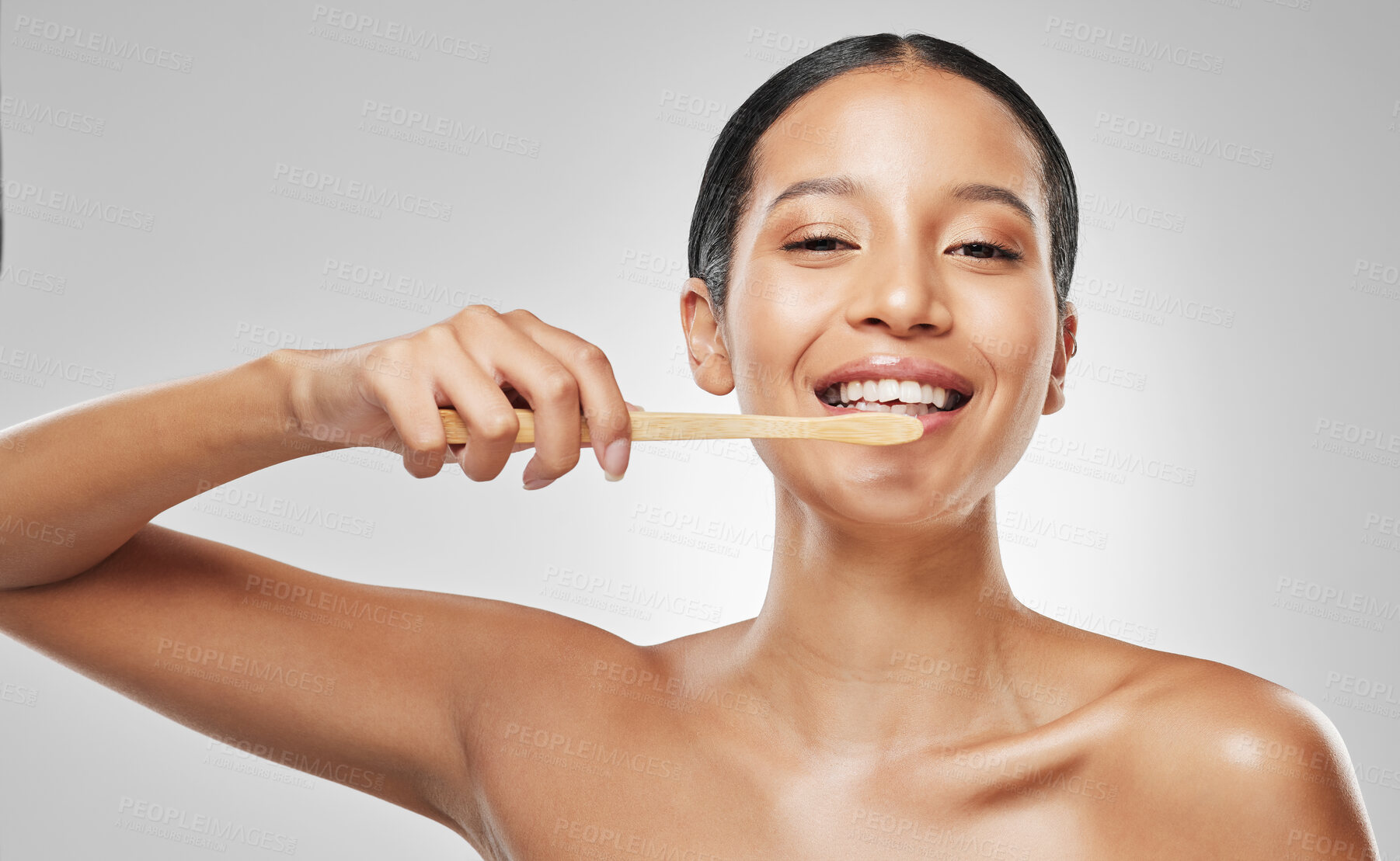 Buy stock photo Studio portrait of an attractive young woman brushing her teeth against a grey background