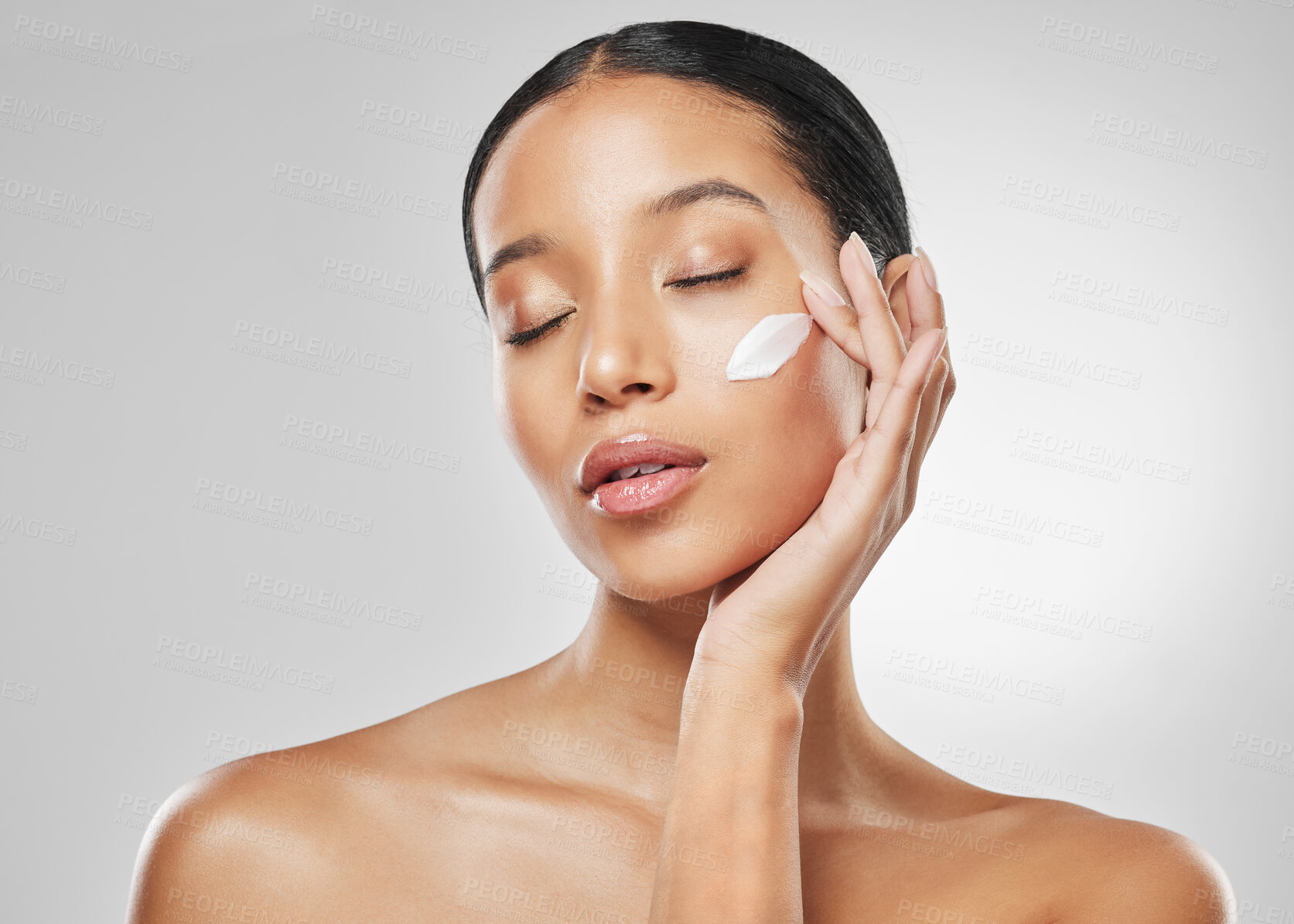 Buy stock photo Studio shot of an attractive young woman posing with moisturiser on her face against a grey background