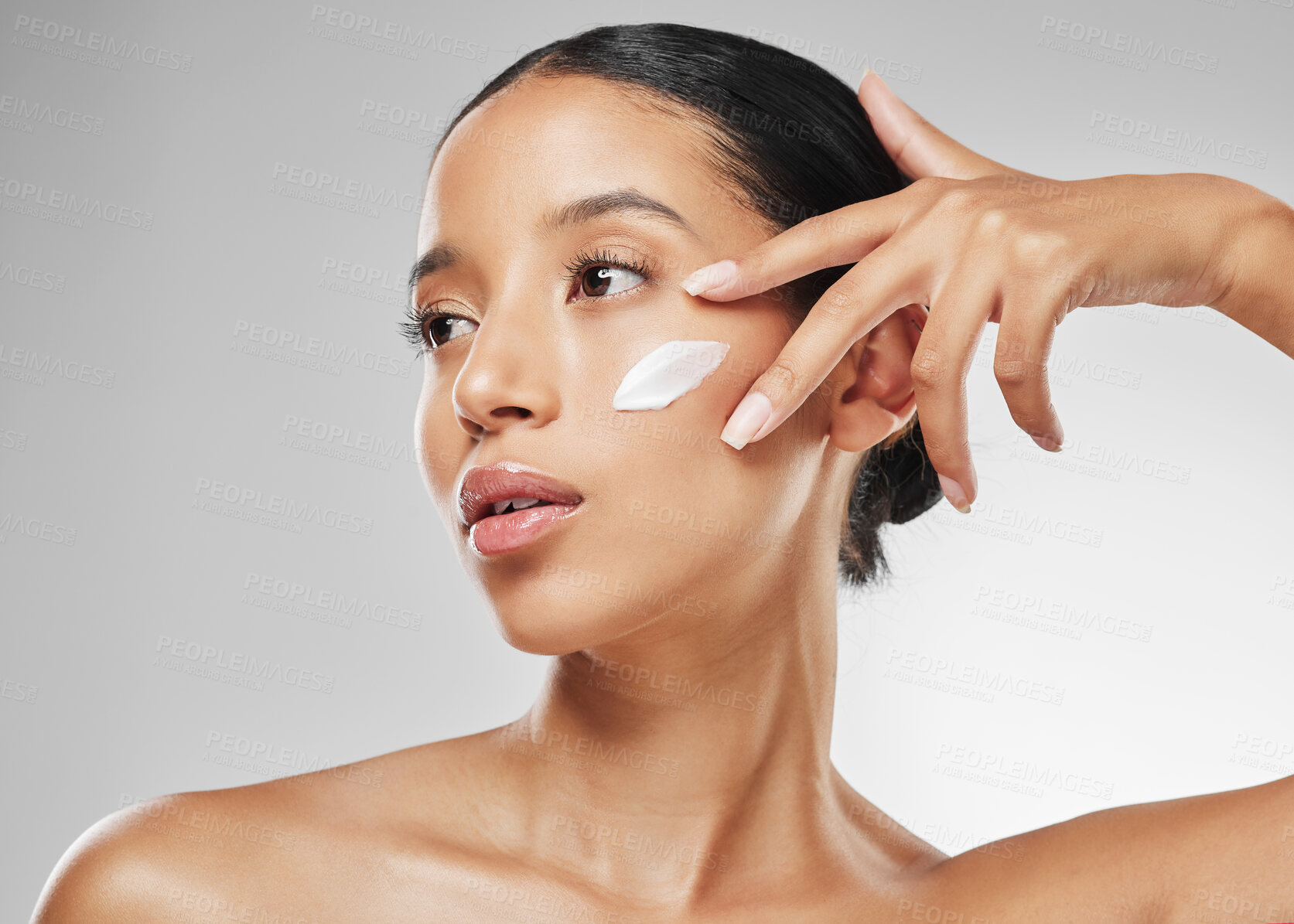 Buy stock photo Studio shot of an attractive young woman posing with moisturiser on her face against a grey background