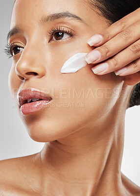 Buy stock photo Studio shot of an attractive young woman posing with moisturiser on her face against a grey background