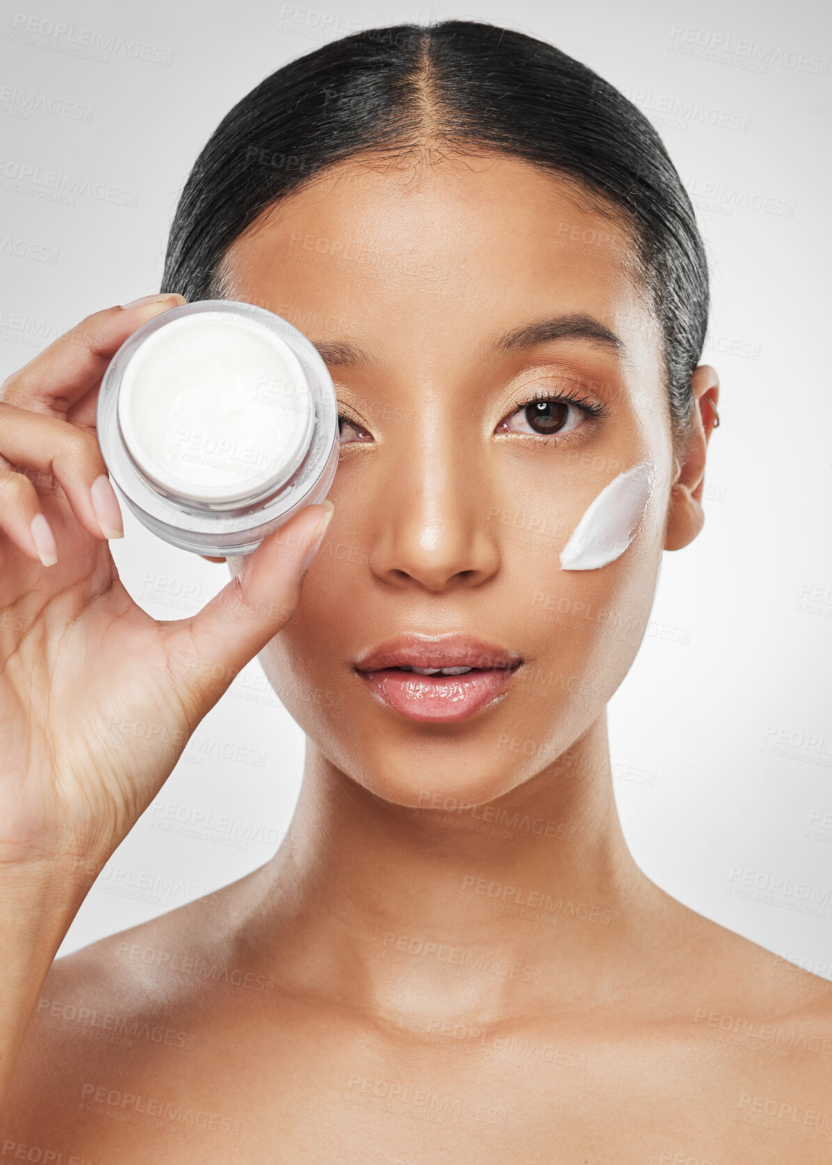 Buy stock photo Studio portrait of an attractive young woman applying moisturiser on her face against a grey background