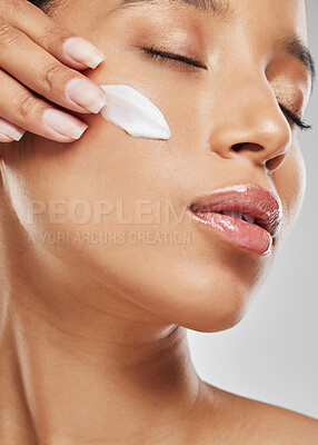 Buy stock photo Studio shot of an attractive young woman applying moisturiser on her face against a grey background