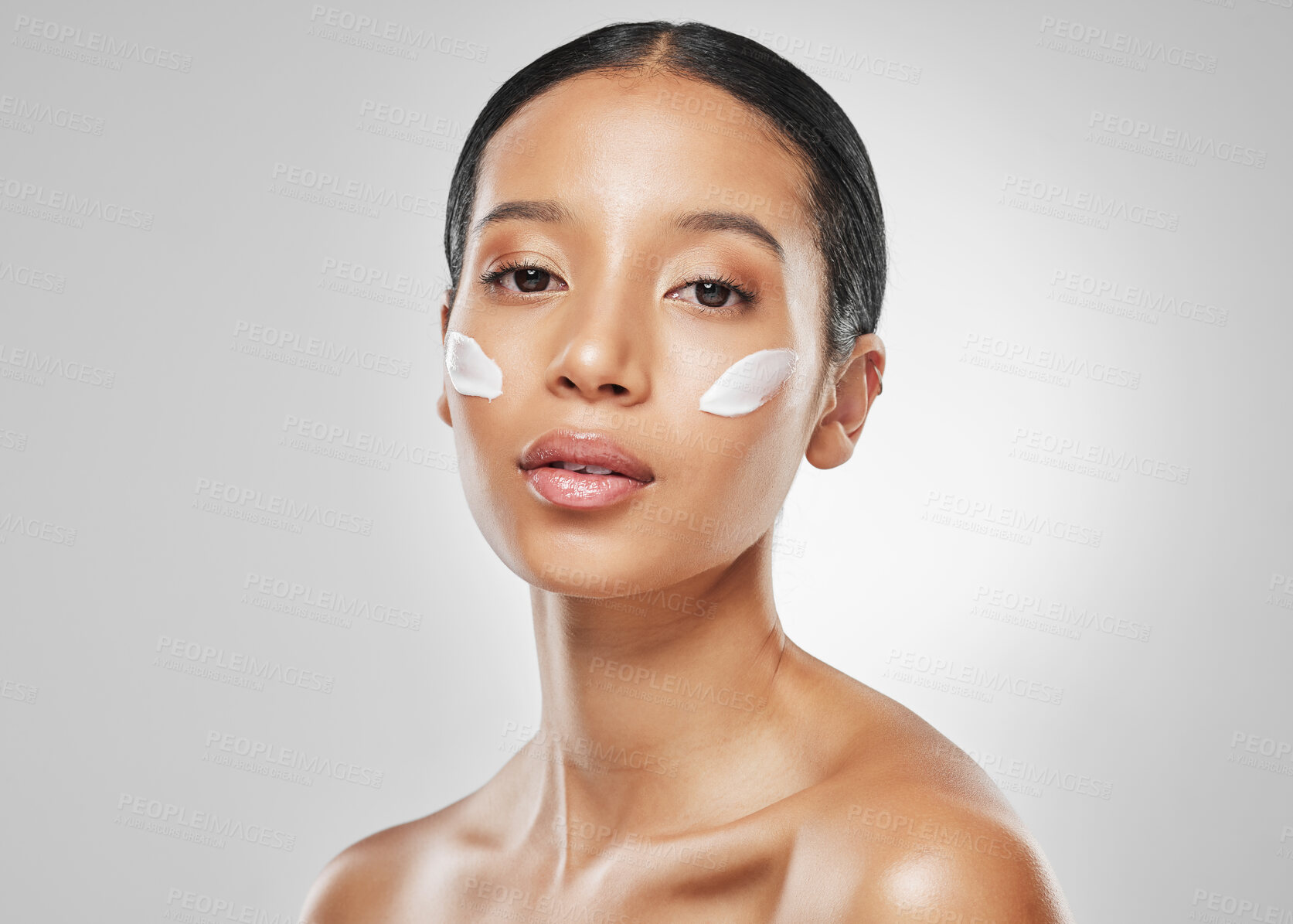 Buy stock photo Studio portrait of an attractive young woman posing with moisturiser on her face against a grey background