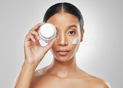 Buy stock photo Studio portrait of an attractive young woman applying moisturiser on her face against a grey background