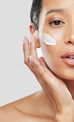 Buy stock photo Studio portrait of an attractive young woman applying moisturiser on her face against a grey background