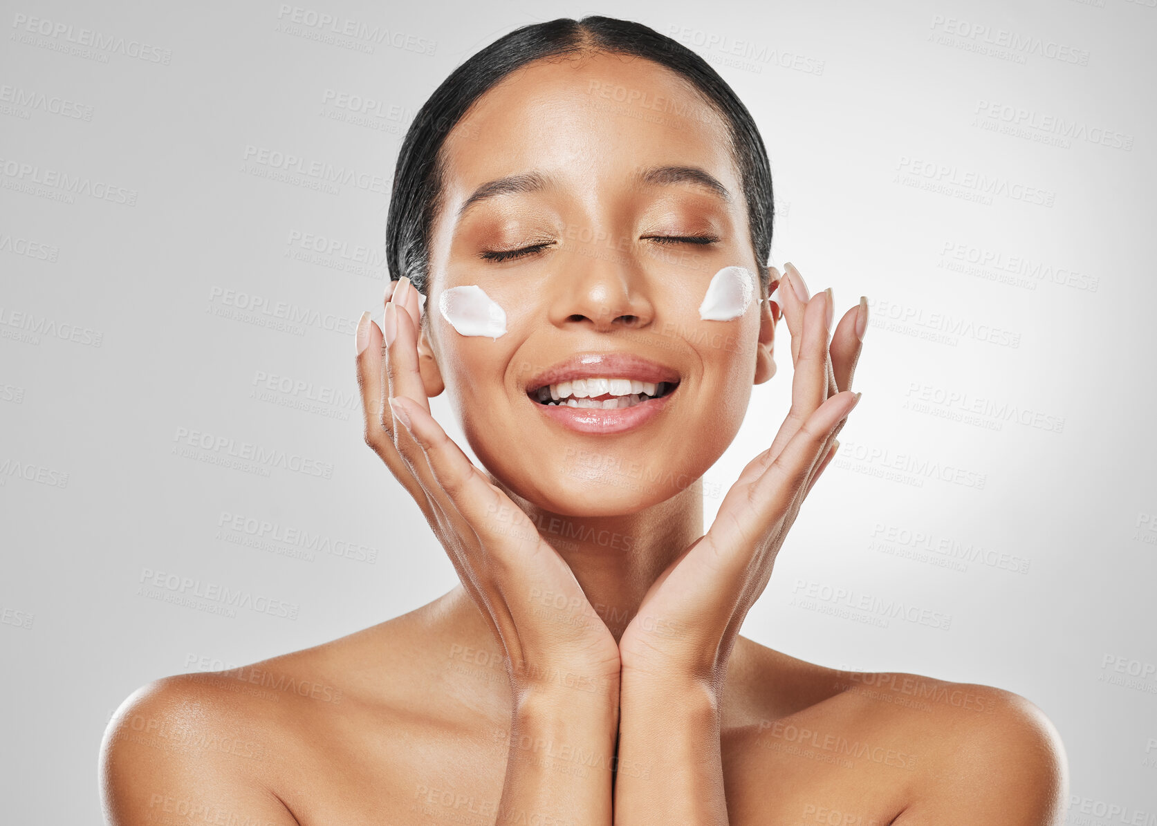 Buy stock photo Studio shot of an attractive young woman applying moisturiser on her face against a grey background