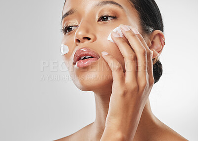 Buy stock photo Studio shot of an attractive young woman applying moisturiser on her face against a grey background