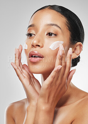 Buy stock photo Studio shot of an attractive young woman applying moisturiser on her face against a grey background