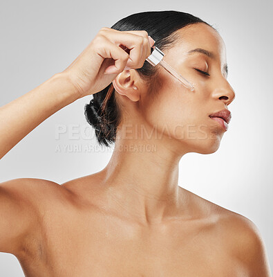 Buy stock photo Studio shot of an attractive young woman applying serum to her face against a grey background