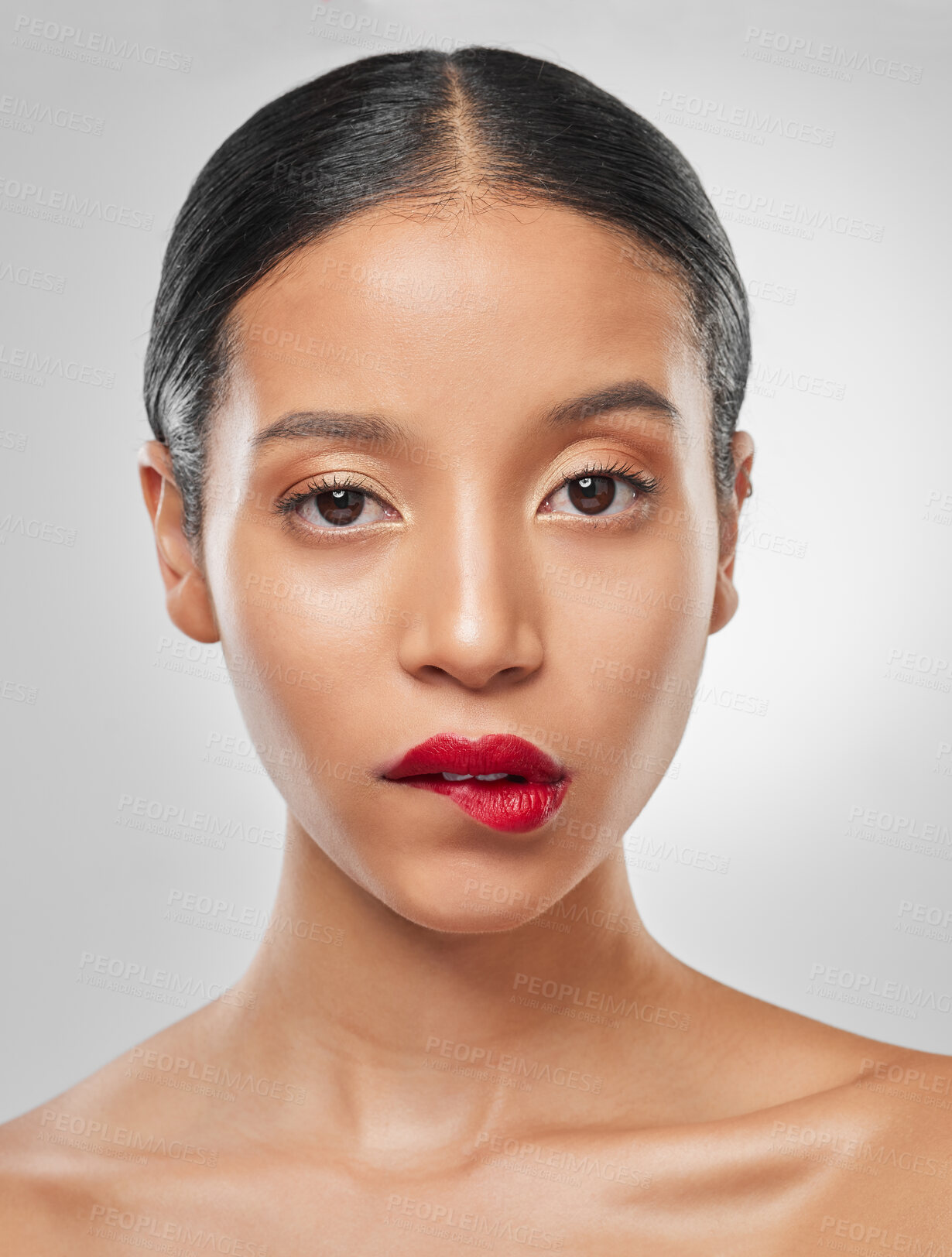 Buy stock photo Studio portrait of an attractive young woman wearing red lipstick and biting her lip against a grey background