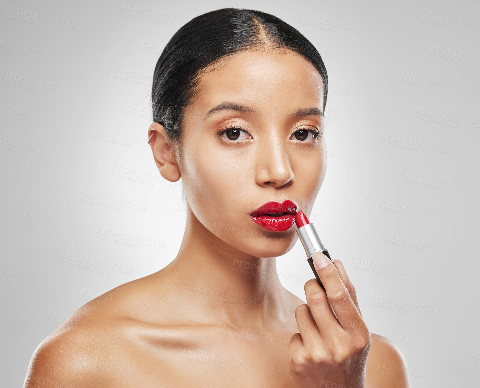 Buy stock photo Studio portrait of a young woman applying red lipstick against a grey background