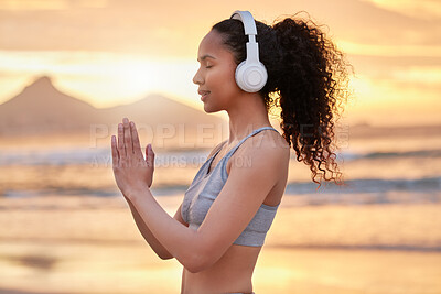 Buy stock photo Shot of a woman wearing headphones while practising yoga on the beach