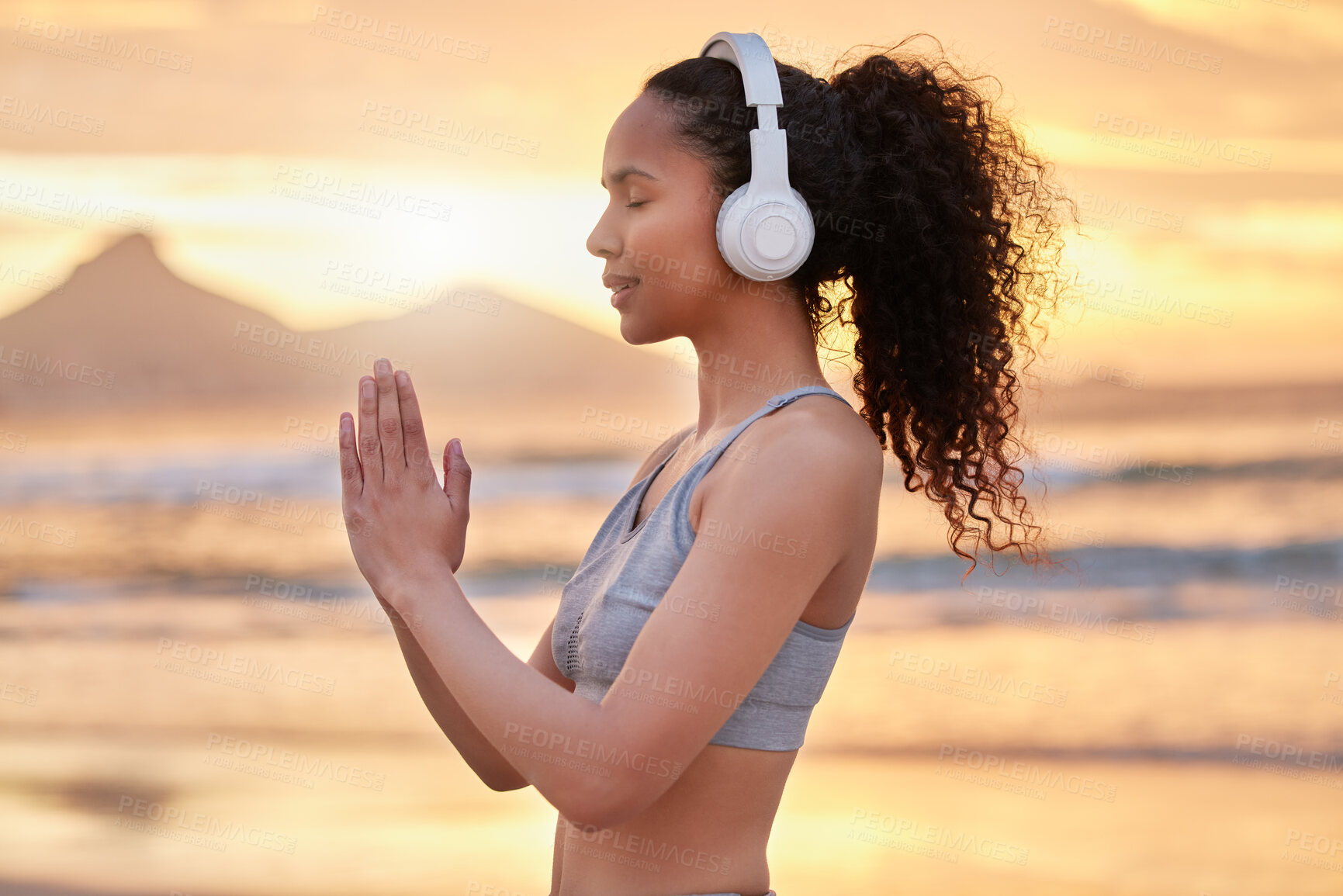 Buy stock photo Shot of a woman wearing headphones while practising yoga on the beach