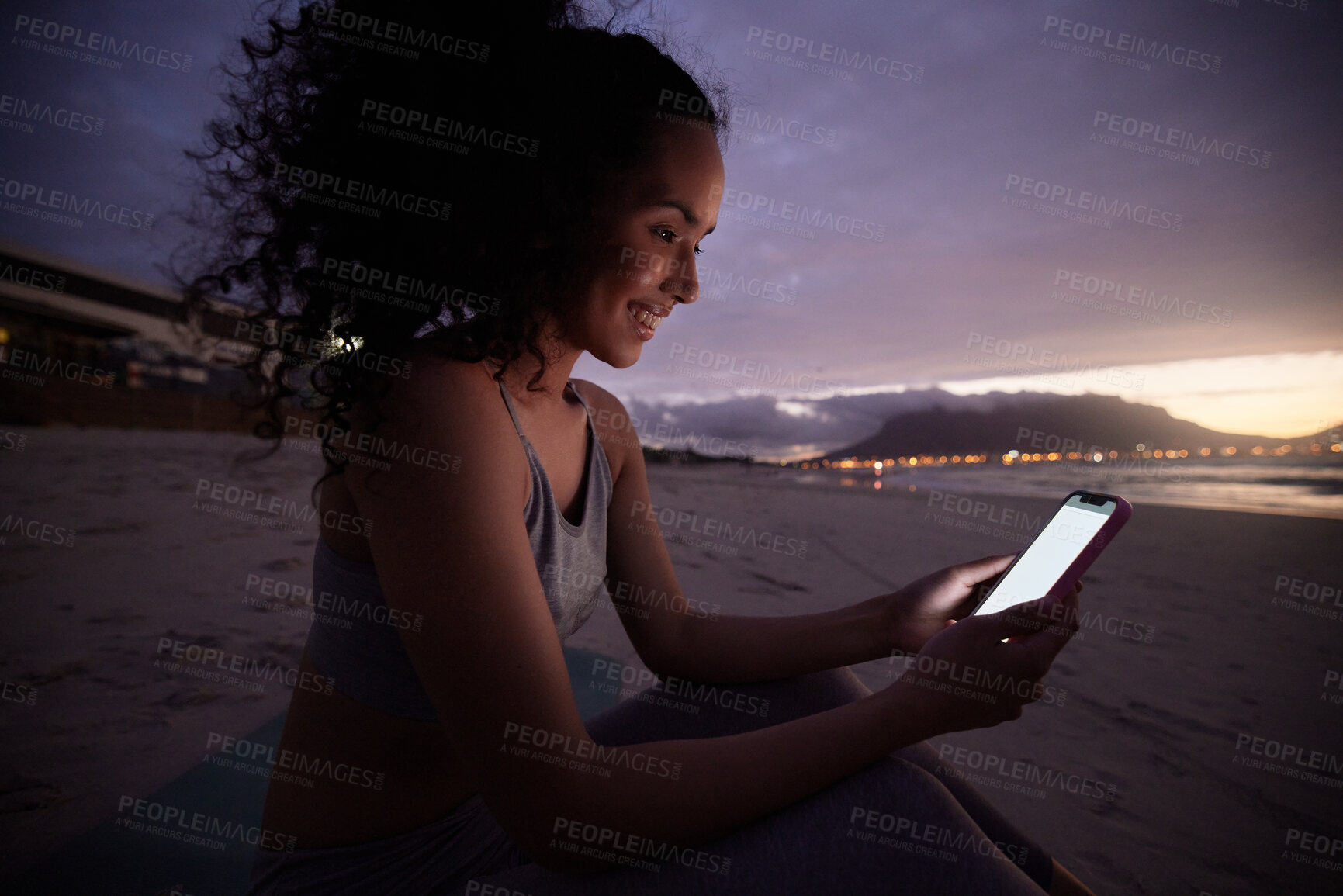 Buy stock photo Woman, phone and fitness at beach, sunset and happy with notification, texting and mockup space on screen. Girl, person and smile with smartphone, reading and mobile app in dark at dusk in Colombia