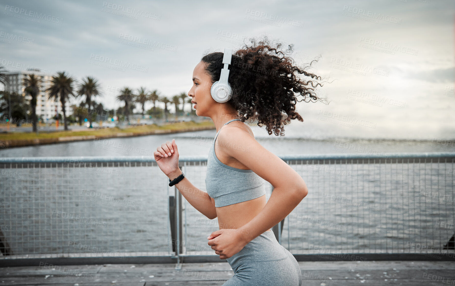Buy stock photo Woman, headphones and running outdoor for fitness, sports and cardio exercise in morning with music. Female person, listening and jog on bridge for health, training and workout with radio or playlist