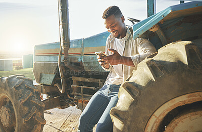 Buy stock photo Shot of a young farmer using a phone while standing against a tractor