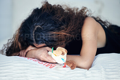 Buy stock photo Shot of a young woman looking sad while holding a teddy bear and lying on a bed alongside a missing person poster