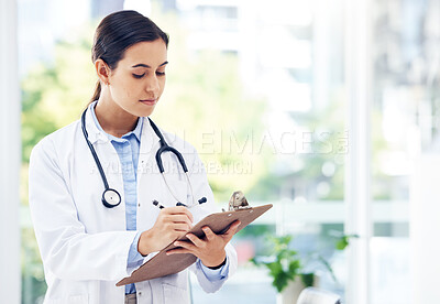 Buy stock photo Shot of a young doctor writing notes on a clipboard in a hospital