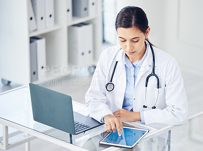 Buy stock photo Shot of a young doctor working on a digital tablet and laptop in a medical office