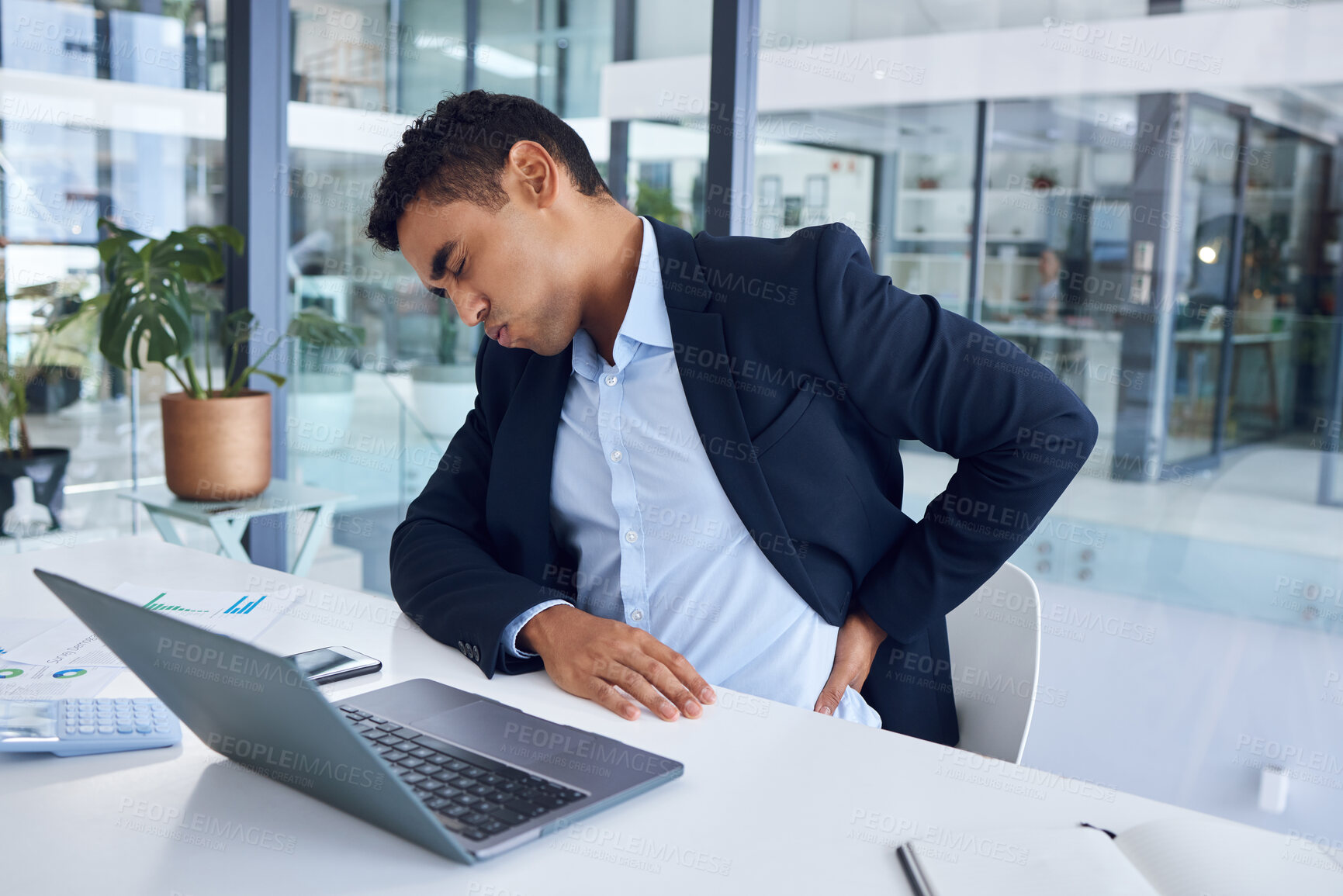 Buy stock photo Shot of a young businessman experiencing back pain while working in an office