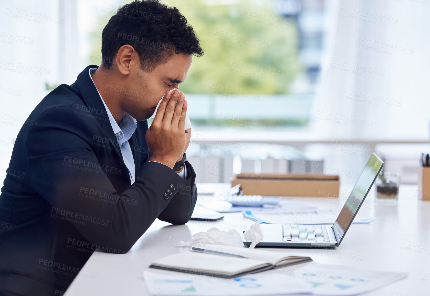 Buy stock photo Shot of a young businessman blowing his nose while working in an office