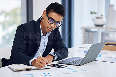Buy stock photo Shot of a young businessman writing notes while working on a laptop in an office