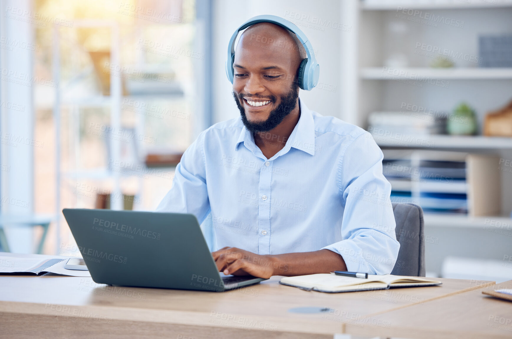 Buy stock photo Shot of a young businessman using a laptop and listening to music in a modern office