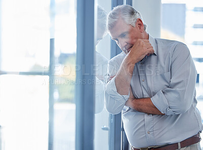 Buy stock photo Shot of a mature businessman looking stressed out while standing at a window in an office