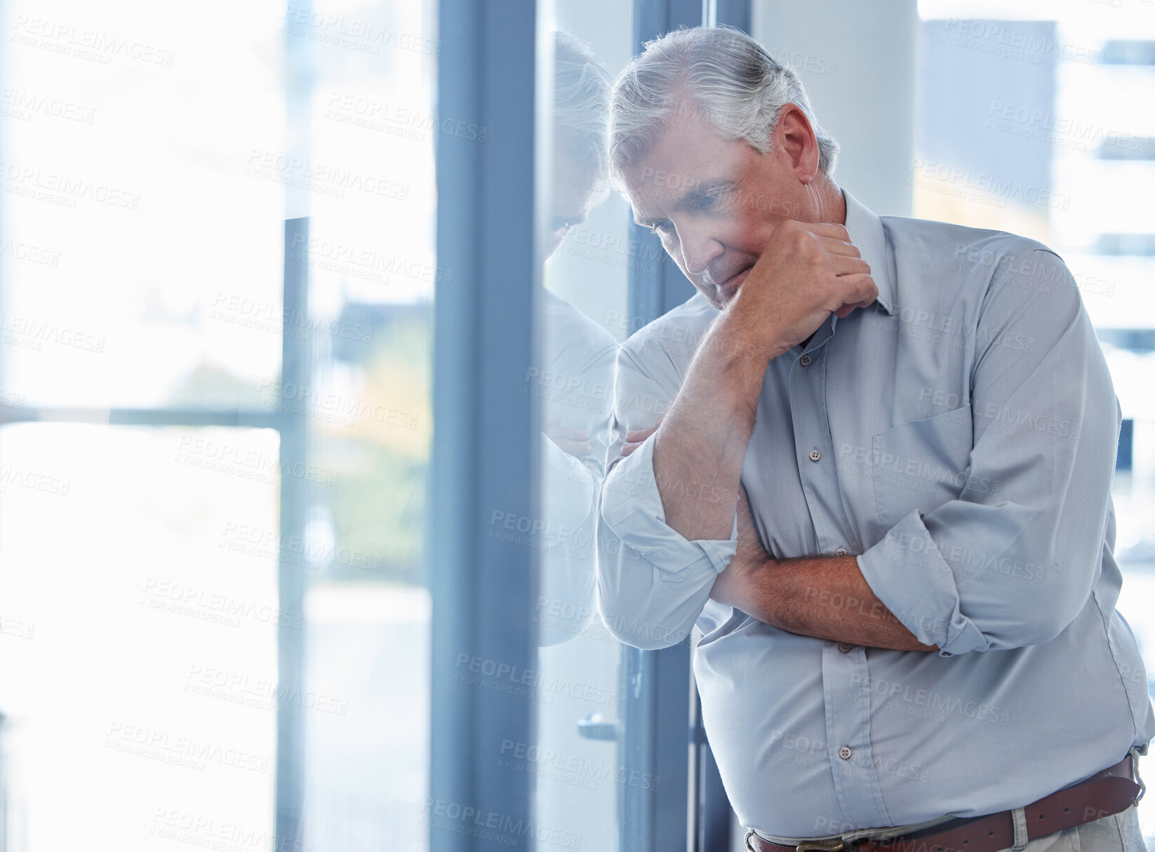 Buy stock photo Shot of a mature businessman looking stressed out while standing at a window in an office