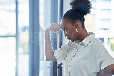 Buy stock photo Shot of a young businesswoman looking stressed out while standing at a window in an office