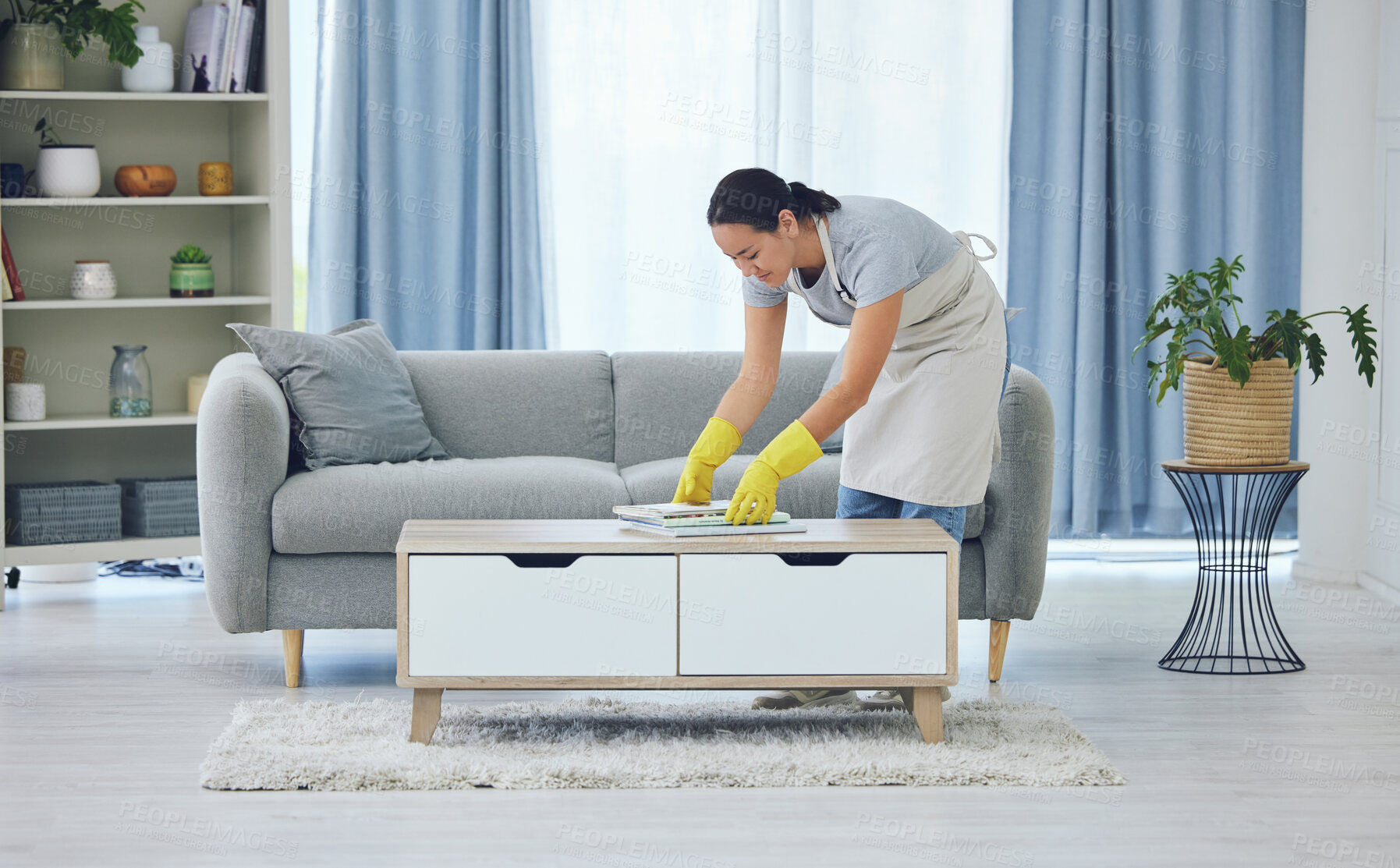 Buy stock photo Cleaning, tidy and woman by table in living room for organising, remove dirt or doing chores. Magazine, gloves and domestic worker with apron for housekeeping, maid service or maintenance in home