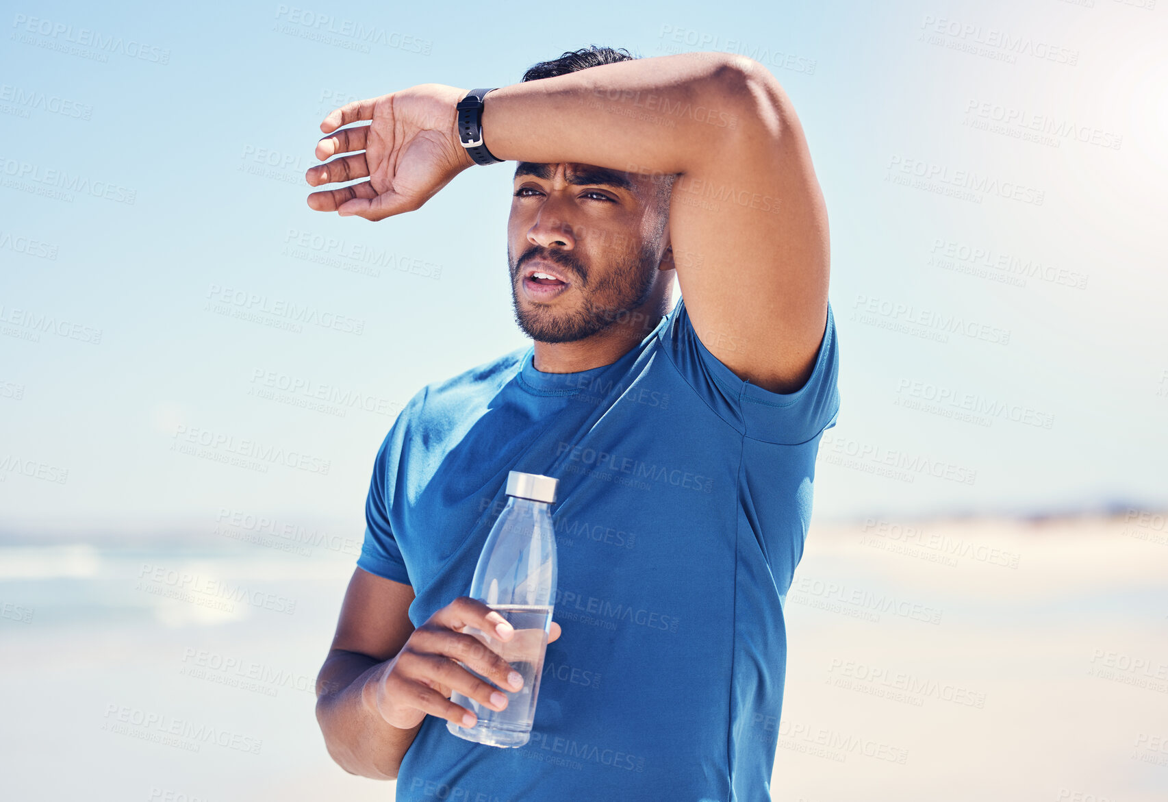 Buy stock photo Shot of a man holding a bottle water while looking exhausted during his run