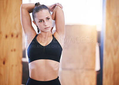 Buy stock photo Shot of a sporty young woman stretching her arms while exercising in a gym