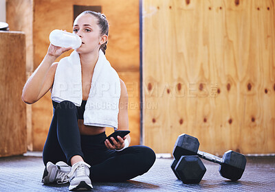 Buy stock photo Shot of a sporty young woman drinking water and using a cellphone while exercising in a gym