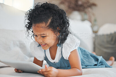 Buy stock photo Shot of an adorable little girl using a digital tablet while relaxing on the sofa at home