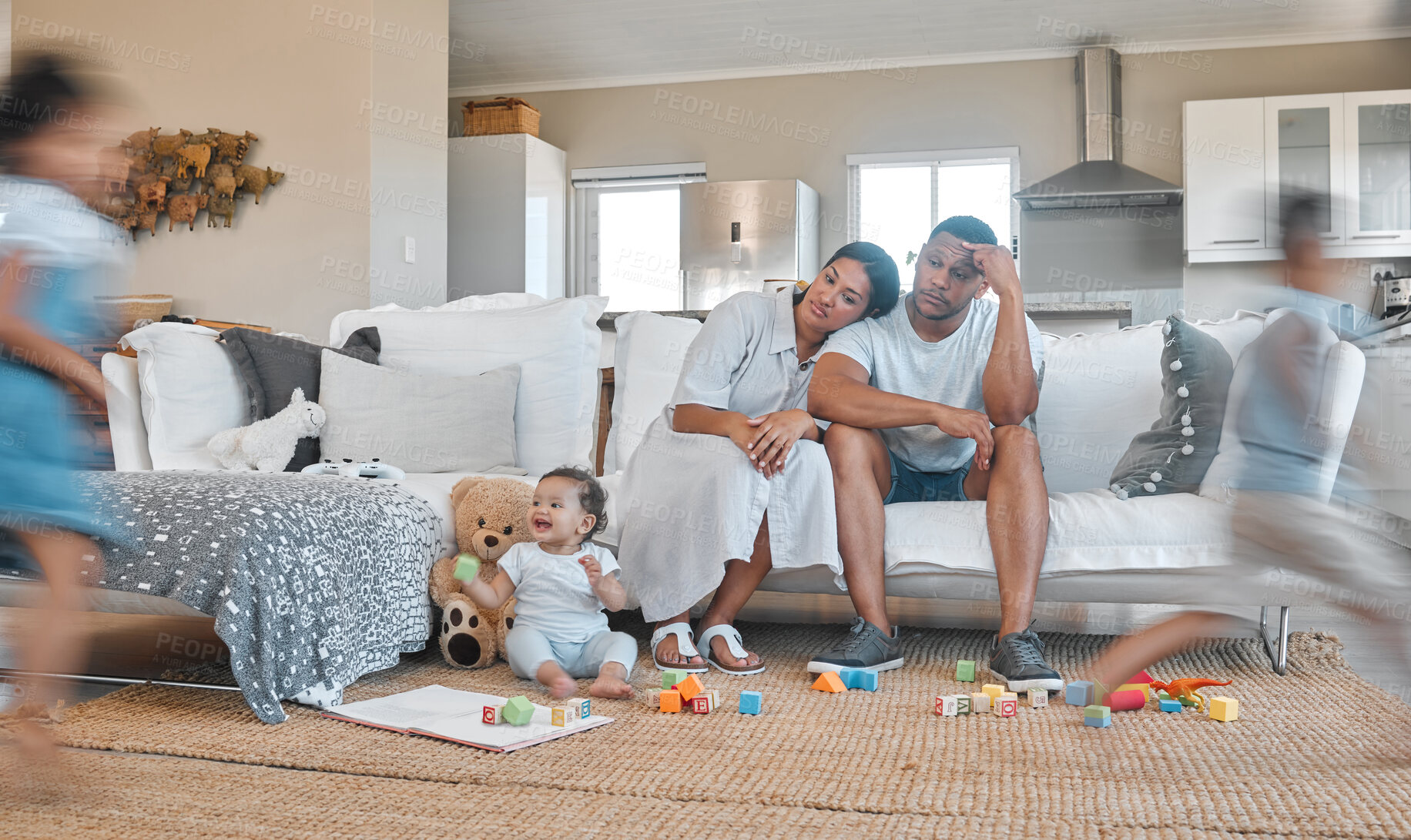 Buy stock photo Shot of a young couple looking stressed at home while their kids play around them