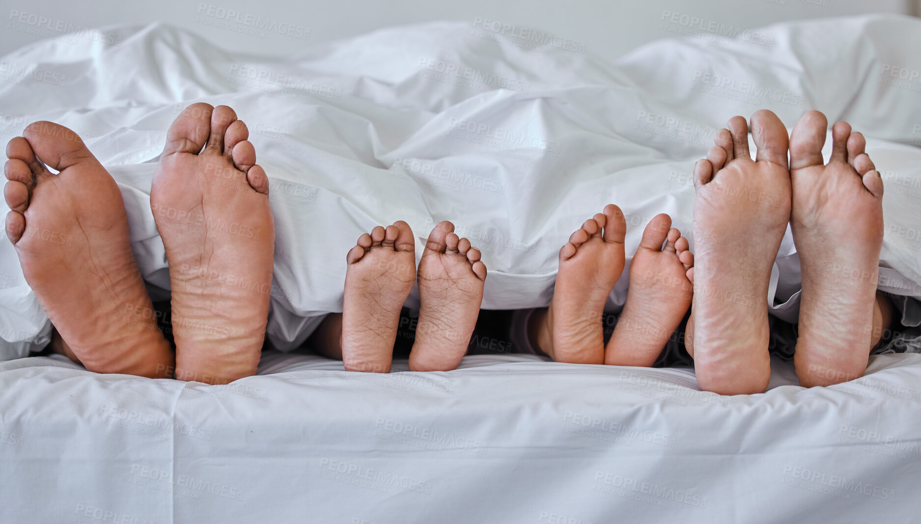 Buy stock photo Shot of a family laying barefoot on a bed at home