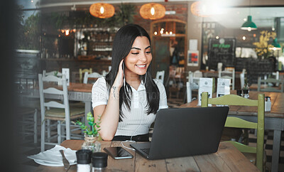 Buy stock photo Shot of a young businesswoman listening to music while working on her laptop in a cafe