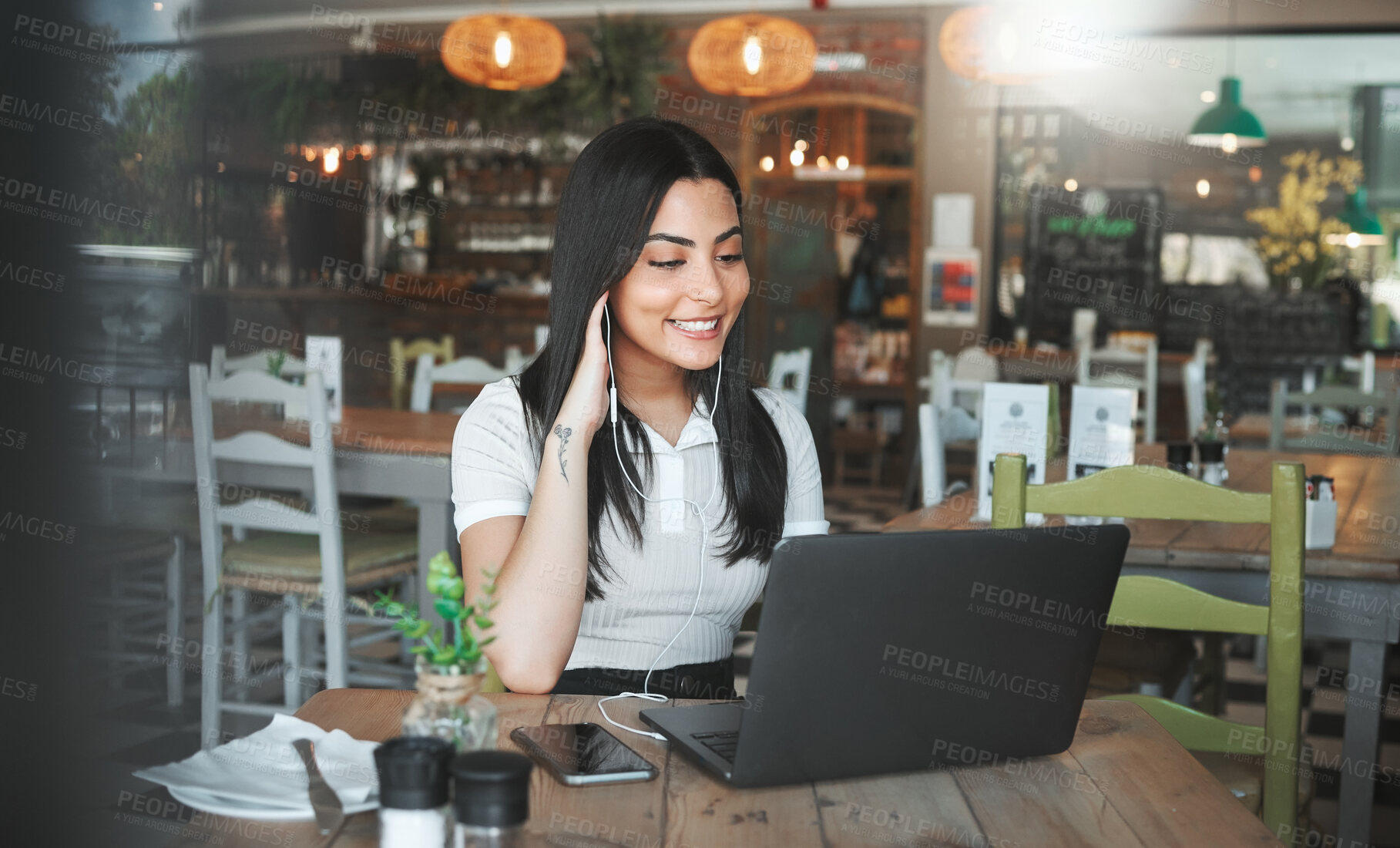 Buy stock photo Shot of a young businesswoman listening to music while working on her laptop in a cafe