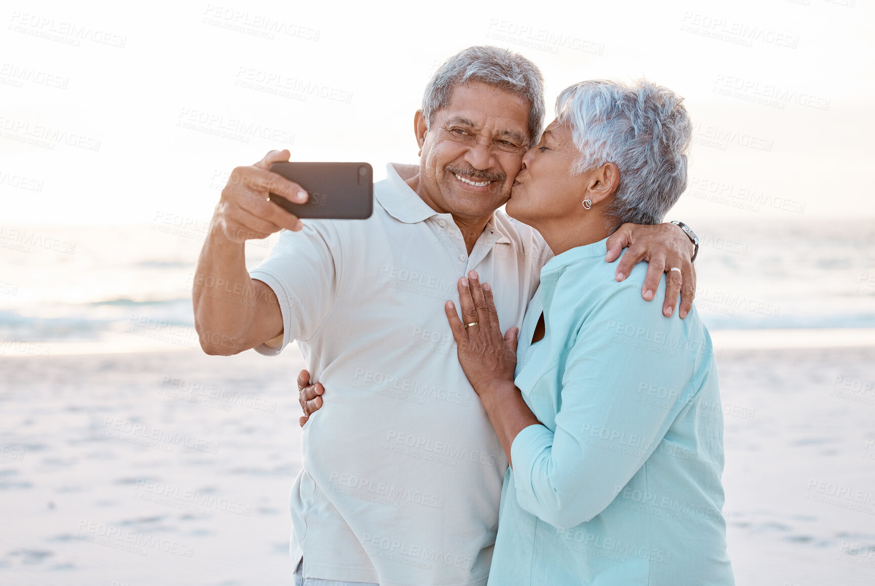 Buy stock photo Senior couple, kiss and beach for selfie, profile picture or online post together in nature. Happy elderly woman kissing man on ocean coast for photo, memory or social media vlog in the outdoors