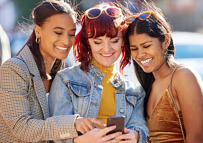 Buy stock photo Cropped shot of three attractive young girlfriends checking a cellphone while out on the town