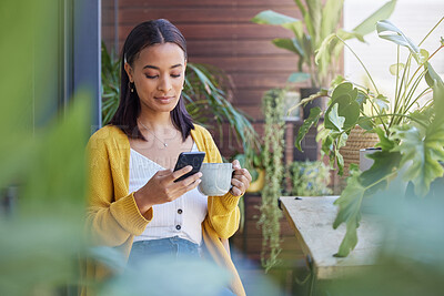 Buy stock photo Shot of a young woman using a phone while drinking coffee on the balcony at home