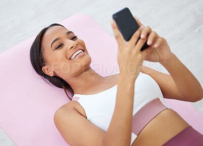 Buy stock photo Shot of a sporty young woman using a cellphone while lying on an exercise mat in a yoga studio