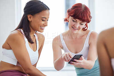 Buy stock photo Shot of two sporty young women looking at something on a cellphone in a yoga studio